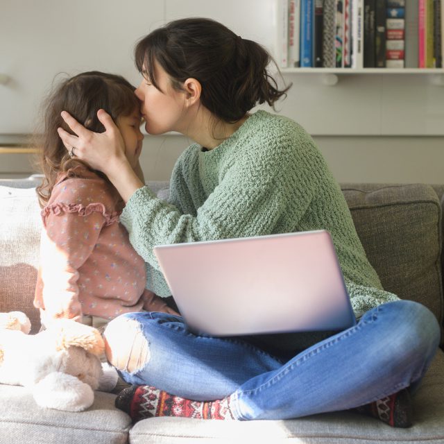 Mom working on laptop on couch, working from home, with daughter